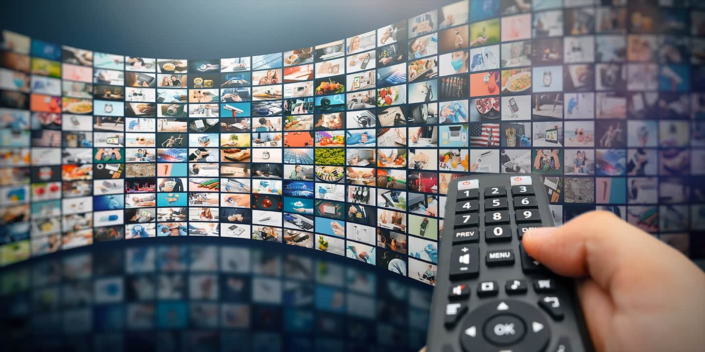 Eine gebogene Wand aus hunderten Fernsehbildern, davor eine Hand mit der Fernbedienung